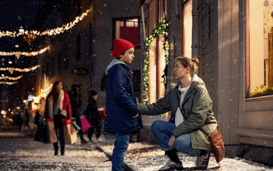 Two people standing on a sidewalk on a Christmas decorated road with snow