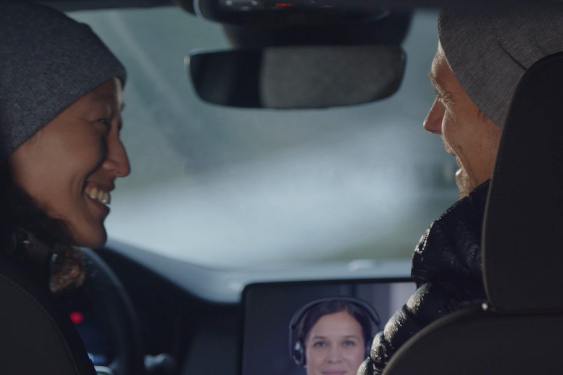Two people facing each other smiling in front seat of car