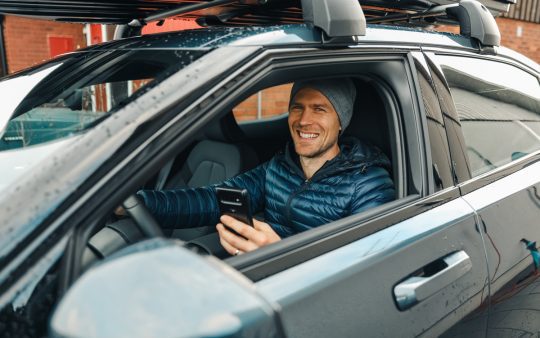 a smiling man holding his phone in a car