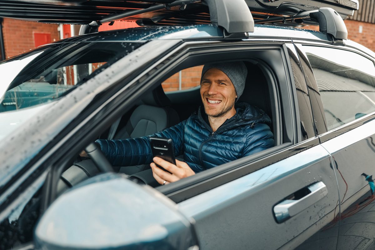 a smiling man holding his phone in a car