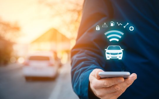 A person with a smartphone on the street, a car in the background, and wireless communication symbols on top of the phone