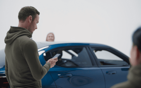 a man looking at his phone next to a car with two women