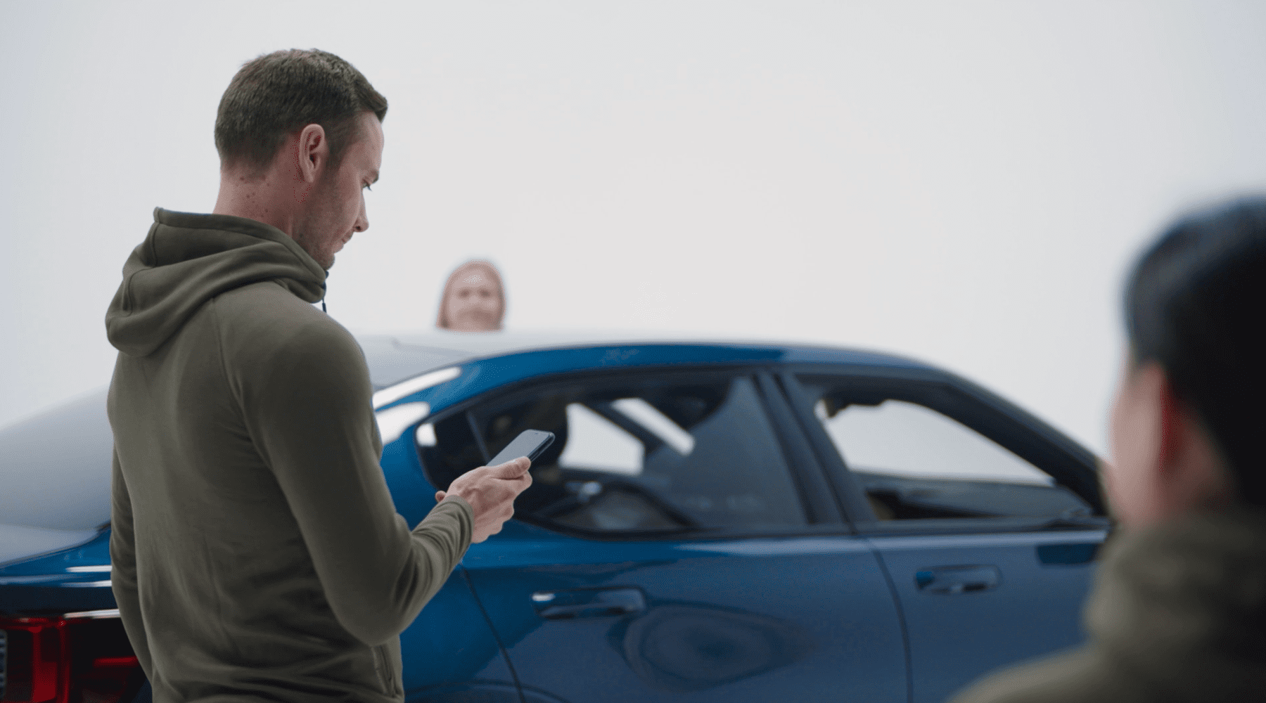 a man looking at his phone next to a car with two women