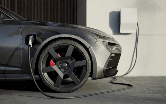 A black electric car charging at home in the drive way.