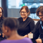 a group of happy people sitting in the office and talking holding coffee cups