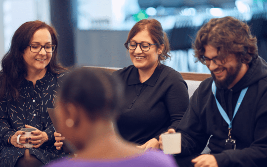 a group of happy people sitting in the office and talking holding coffee cups