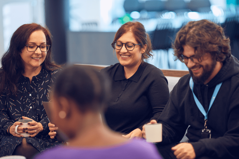 a group of happy people sitting in the office and talking holding coffee cups