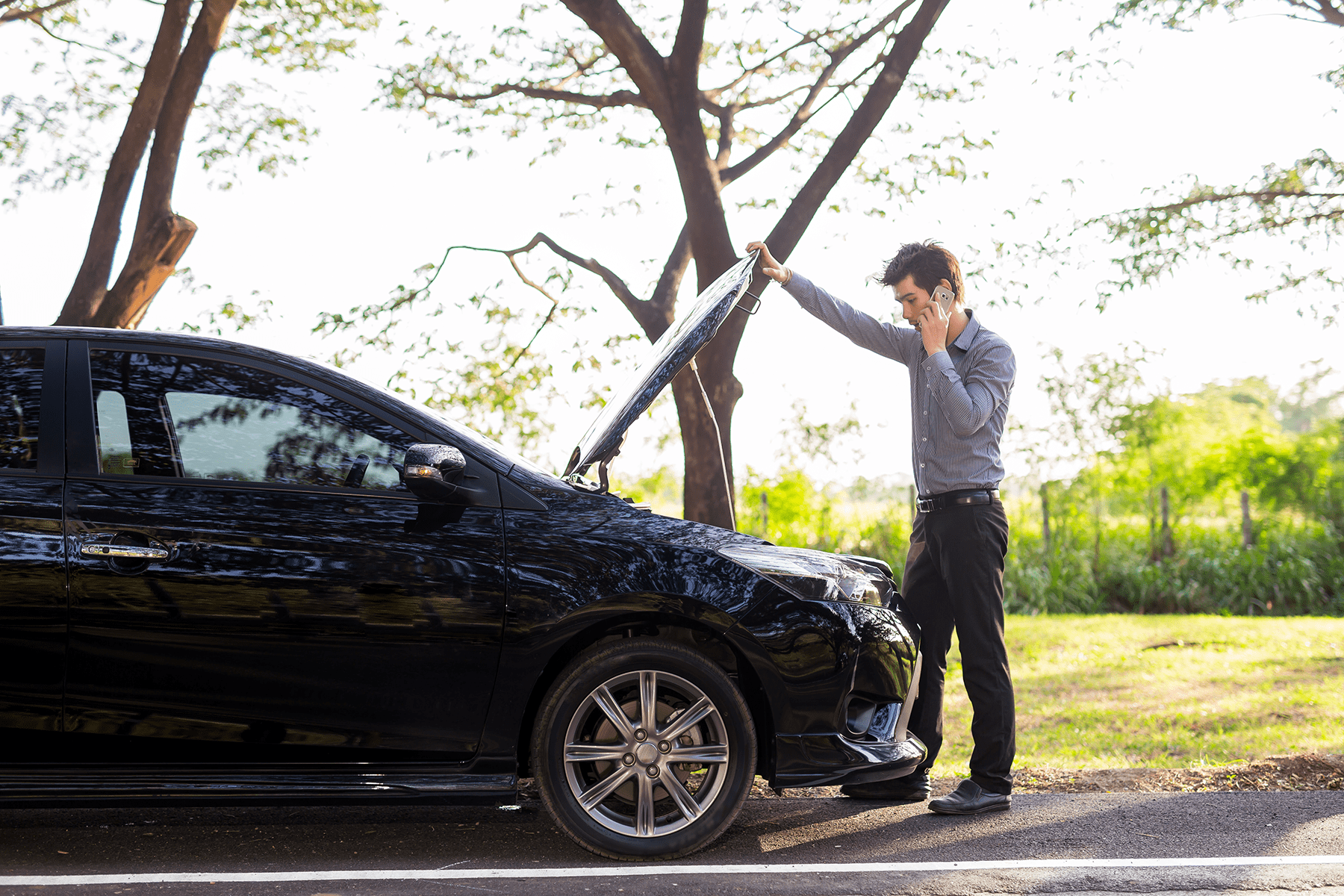 a man talking on a cell phone by a broken car on country road
