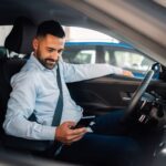 Man in car smiling while connecting smartphone.