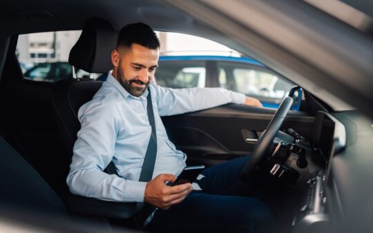 Man in car smiling while connecting smartphone.